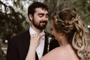 A bride straightening the smiling groom's bow tie on their wedding day.