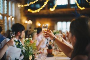 Guests sitting at a wedding table with flowers while toasting the bride and groom.